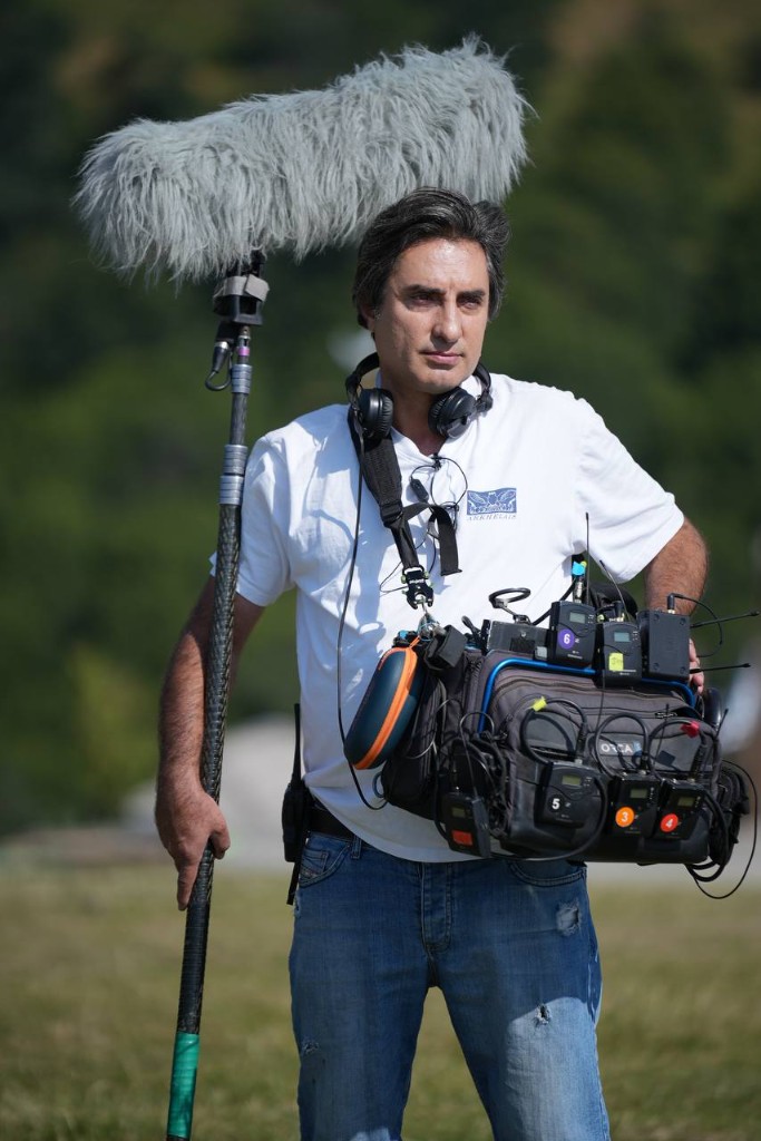 Morteza Najaflo on location with boom pole and sound bag, mountains behind him.