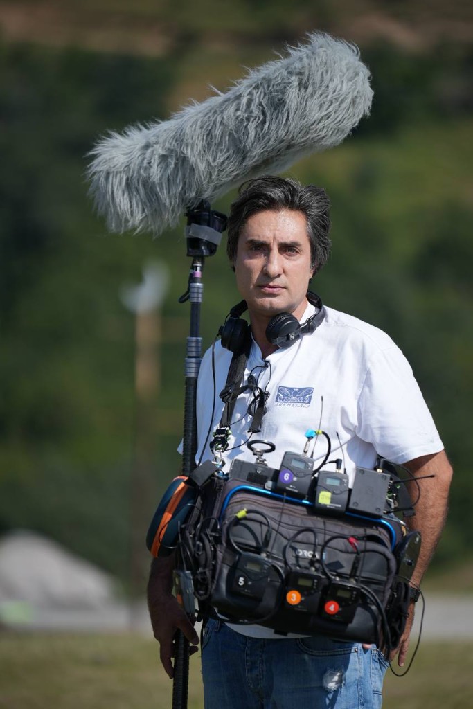 Morteza Najaflo holding the boom overhead while wearing the sound bag on set.
