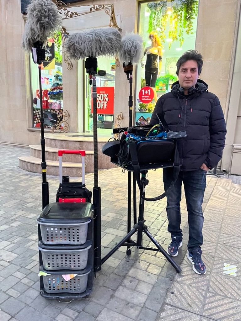 Morteza Najaflo with headphones beside the full sound cart, boom poles, and mixer bag on a city sidewalk
